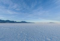 two people standing in a snow field with mountains behind them in the distance in blue skies