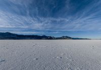 the view of snow capped mountains from a field in the distance, with tracks of footprints on the ground