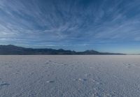 the view of snow capped mountains from a field in the distance, with tracks of footprints on the ground