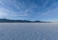 the view of snow capped mountains from a field in the distance, with tracks of footprints on the ground