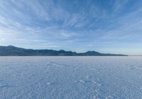 the view of snow capped mountains from a field in the distance, with tracks of footprints on the ground