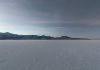 a man with a backpack walking across some snow field next to mountains in the distance