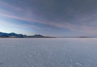 a man with a backpack walking across some snow field next to mountains in the distance