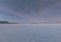 a man with a backpack walking across some snow field next to mountains in the distance