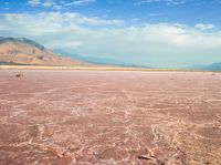 a man standing on the beach, looking out at a vast landscape that includes hills and hills