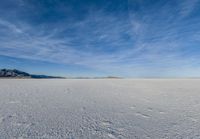 an image of a big field with some snow on it in winter time in the distance, clouds, hills and mountains are seen in the distance