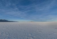 an image of a big field with some snow on it in winter time in the distance, clouds, hills and mountains are seen in the distance