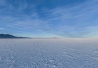 an image of a big field with some snow on it in winter time in the distance, clouds, hills and mountains are seen in the distance