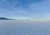 an image of a big field with some snow on it in winter time in the distance, clouds, hills and mountains are seen in the distance