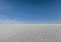 a kite flying through a blue sky over a large snow field under a clear sky