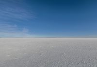 a kite flying through a blue sky over a large snow field under a clear sky