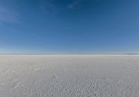 a kite flying through a blue sky over a large snow field under a clear sky