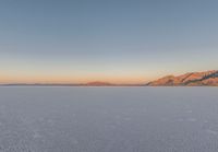 a lone skier in the middle of a salt flat landscape at dusk, with mountains in the distance