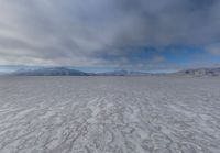 there is a very wide flat surface with snow on it's ground and mountains in the distance