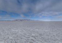 there is a very wide flat surface with snow on it's ground and mountains in the distance