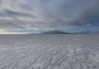 there is a very wide flat surface with snow on it's ground and mountains in the distance