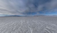 there is a very wide flat surface with snow on it's ground and mountains in the distance