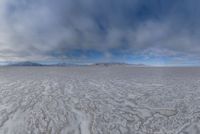 there is a very wide flat surface with snow on it's ground and mountains in the distance