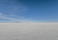 a plane flying over a snow field with mountains and a blue sky in the background