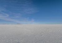 a plane flying over a snow field with mountains and a blue sky in the background