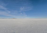 a plane flying over a snow field with mountains and a blue sky in the background