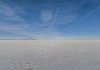 a plane flying over a snow field with mountains and a blue sky in the background