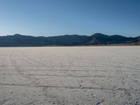 a desert with many rocky mountains in the background and water running across it from them