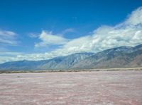 the pink color is the salt in the desert with hills and clouds above it and the sky has fluffy white wispy clouds