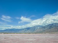 the pink color is the salt in the desert with hills and clouds above it and the sky has fluffy white wispy clouds