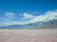 the pink color is the salt in the desert with hills and clouds above it and the sky has fluffy white wispy clouds