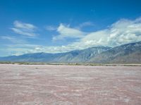 the pink color is the salt in the desert with hills and clouds above it and the sky has fluffy white wispy clouds