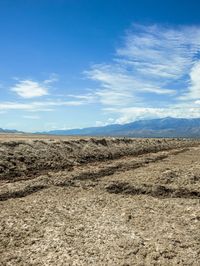 a dirt road going through an empty dry plain with mountains in the background on a clear day