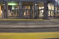 the side walk near the street with people walking by at dusk and yellow light from the lights illuminating the entrance
