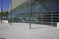 a big building with glass windows is sitting empty in the daytime, along with a bench on the sidewalk and the sun shining behind it