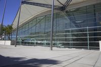 a big building with glass windows is sitting empty in the daytime, along with a bench on the sidewalk and the sun shining behind it