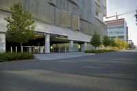 an empty street with an urban building in the background and trees and shrubs lining both sides of it