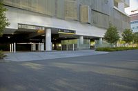 an empty street with an urban building in the background and trees and shrubs lining both sides of it
