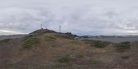 a large hill is overlooking some buildings and a road near by with clouds overhead in the sky