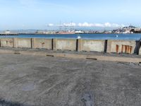 a concrete bench sitting in front of a water view with some empty bins on the ground