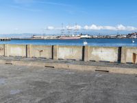 a concrete bench sitting in front of a water view with some empty bins on the ground