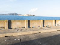 a concrete bench sitting in front of a water view with some empty bins on the ground