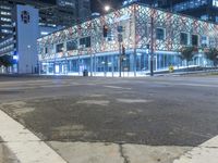 an empty street near a building at night with no traffic lights in the foreground