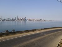 a view of the ocean from a highway in the distance, with the city skyline in the background