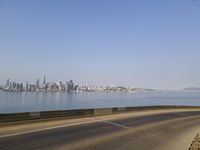 a view of the ocean from a highway in the distance, with the city skyline in the background