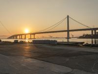 two men with skateboards stand in front of the water near the bridge as the sun sets