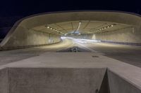 the concrete structure looks like a tunnel with a road in it at night time with lights on the sides