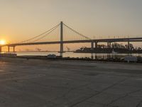 a bridge is seen in the distance at sunset near water and land, with a concrete area