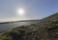 the sun shines in front of a highway near a mountain top with a long bridge