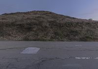 a parking lot with a steep mountain in the background and sky above it and a yellow sign painted in white on the ground