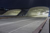 an empty highway at night time with the lights on and a view of mountains in the distance